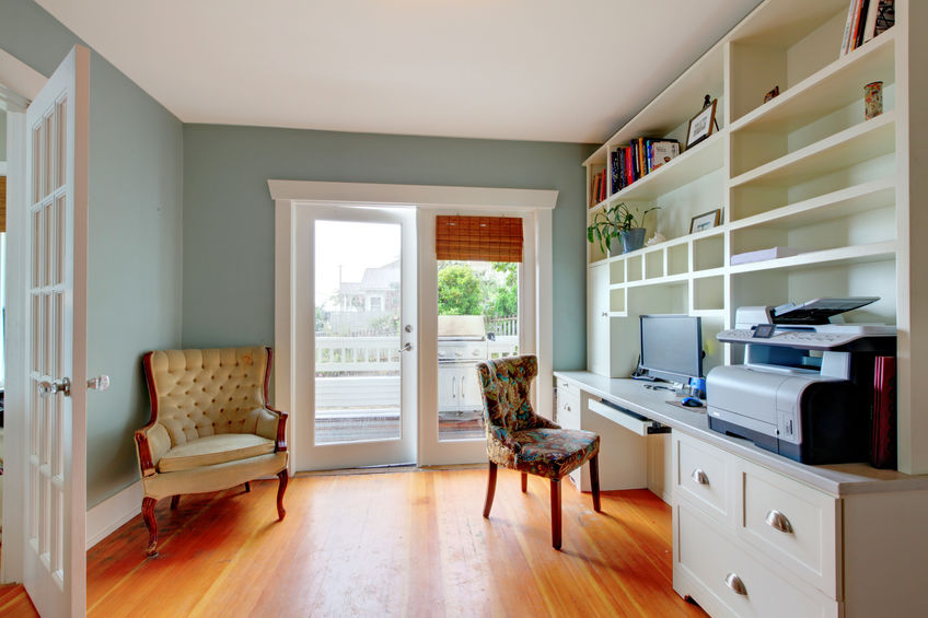 Home office with white open shelves, hardwood floor and blue walls.