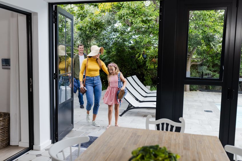 Family entering vacation home from patio, smiling and enjoying sunny day together.