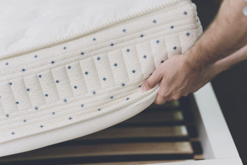 Man lifting up bed mattress to check the condition of the bed frame