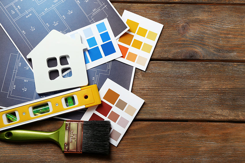 Color samples, decorative house, gloves, and paintbrushes on wooden table background