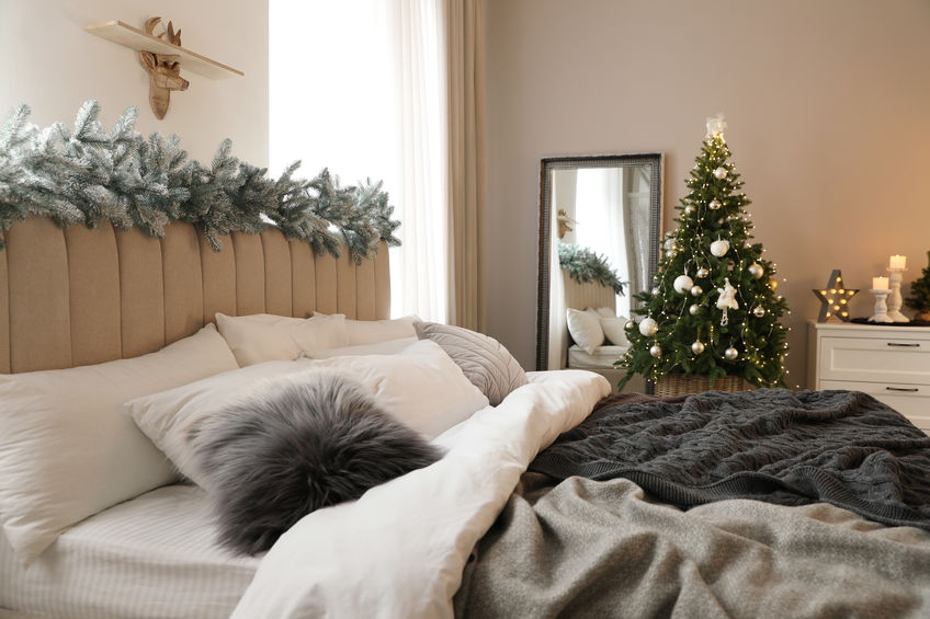 Beautiful decorated Christmas tree with fairy lights in bedroom interior